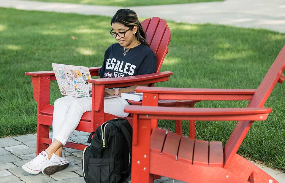 student doing classwork outdoors on an Adirondack chair