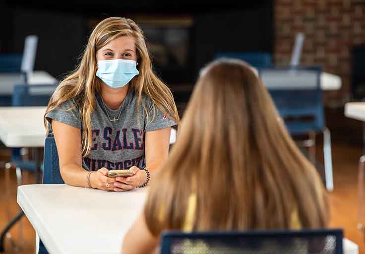 masked students talking at table