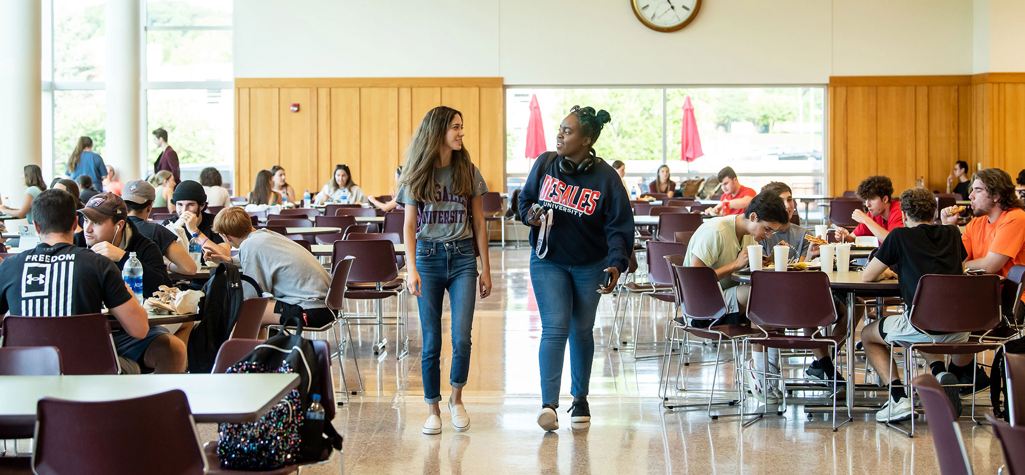 Two DeSales University students walking, smiling, and talking in the cafeteria.