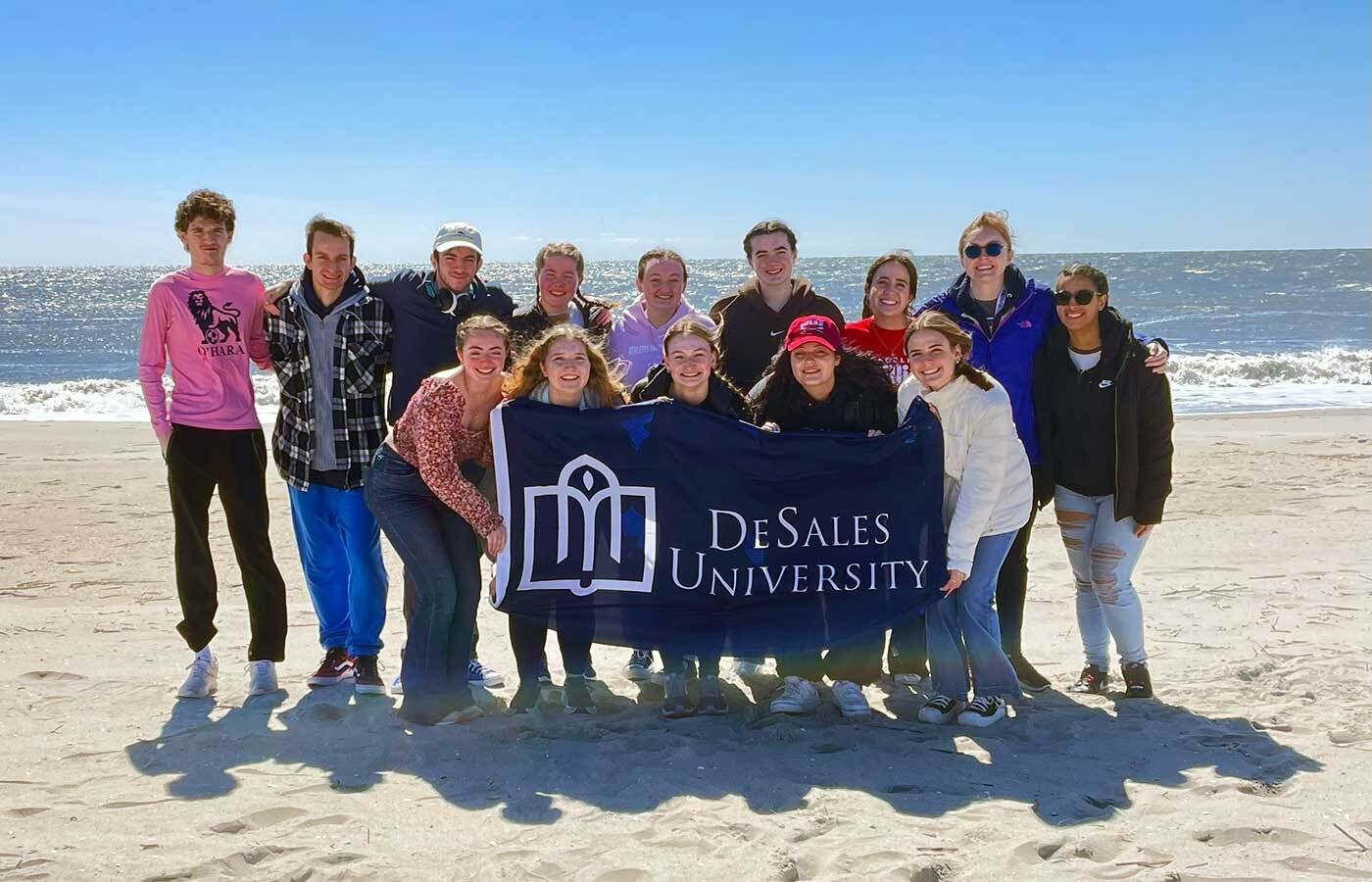 Students on beach holding DeSales flag during First-Year Leadership Summit