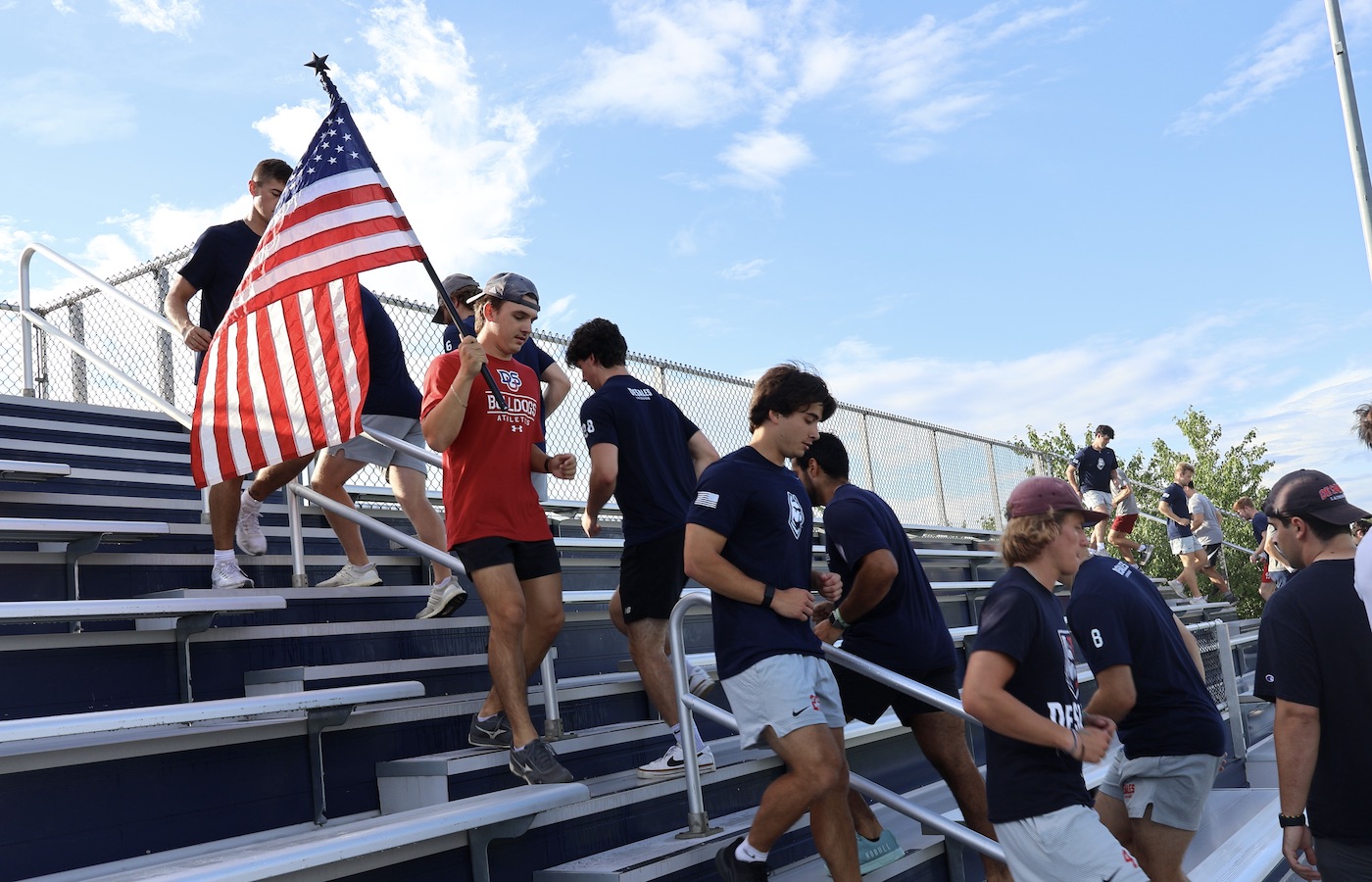Lacrosse players running up bleacher steps, holding flag