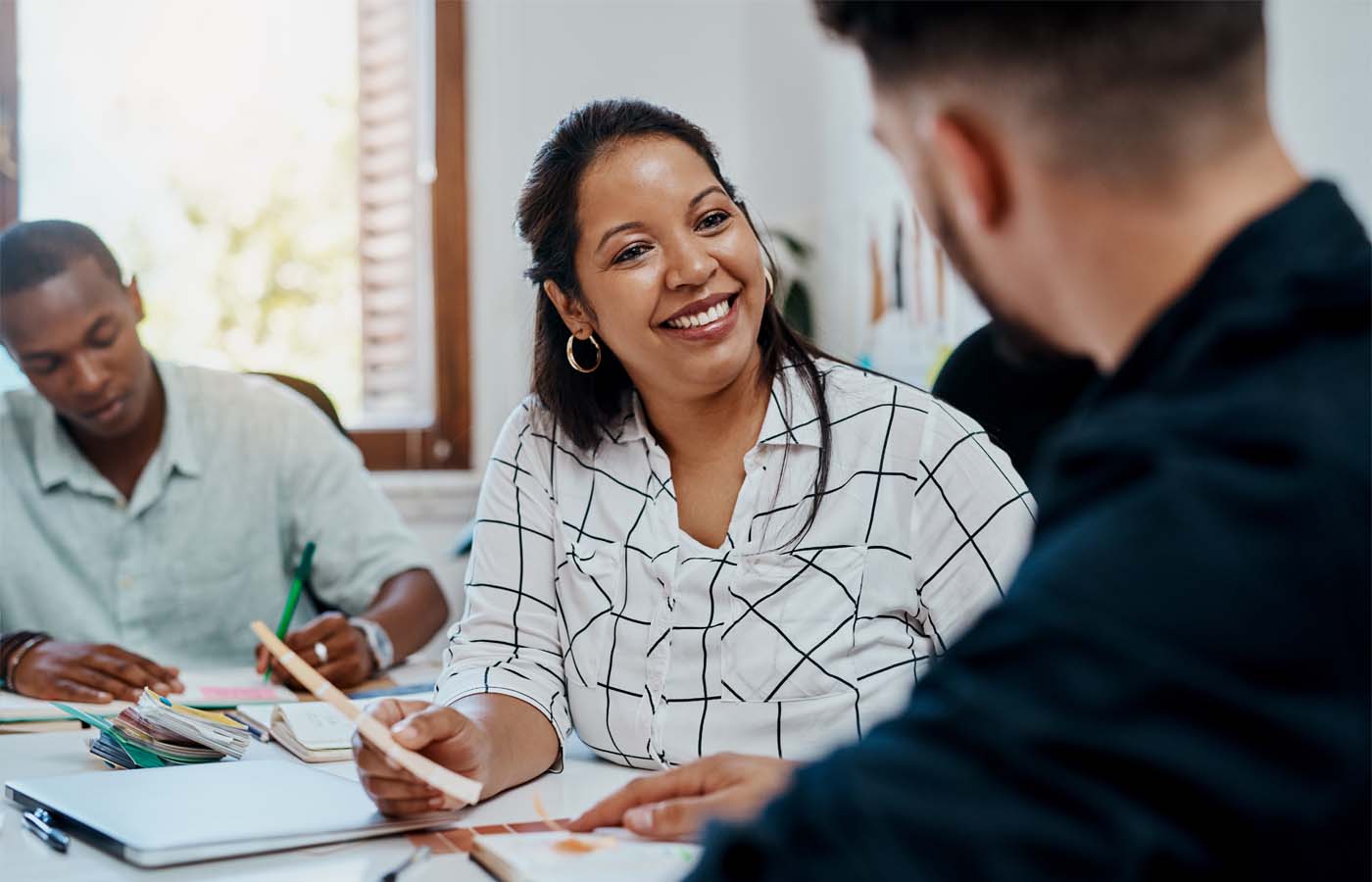Smiling woman engaging in conversation with two other adults in a classroom setting, highlighting a collaborative learning environment for adult students